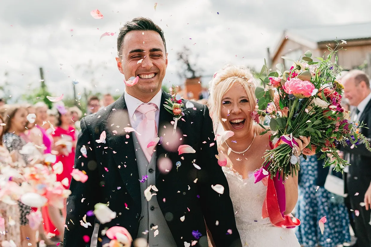 Couple with real petal confetti after indoor ceremony at barn wedding venue in Warwickshire