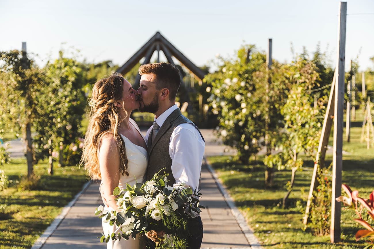 Bride and groom kissing on the path of espalier apple trees
