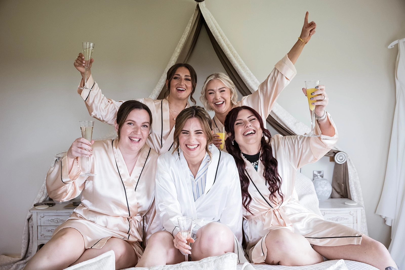 Bridesmaids and bride on the bed raising a toast